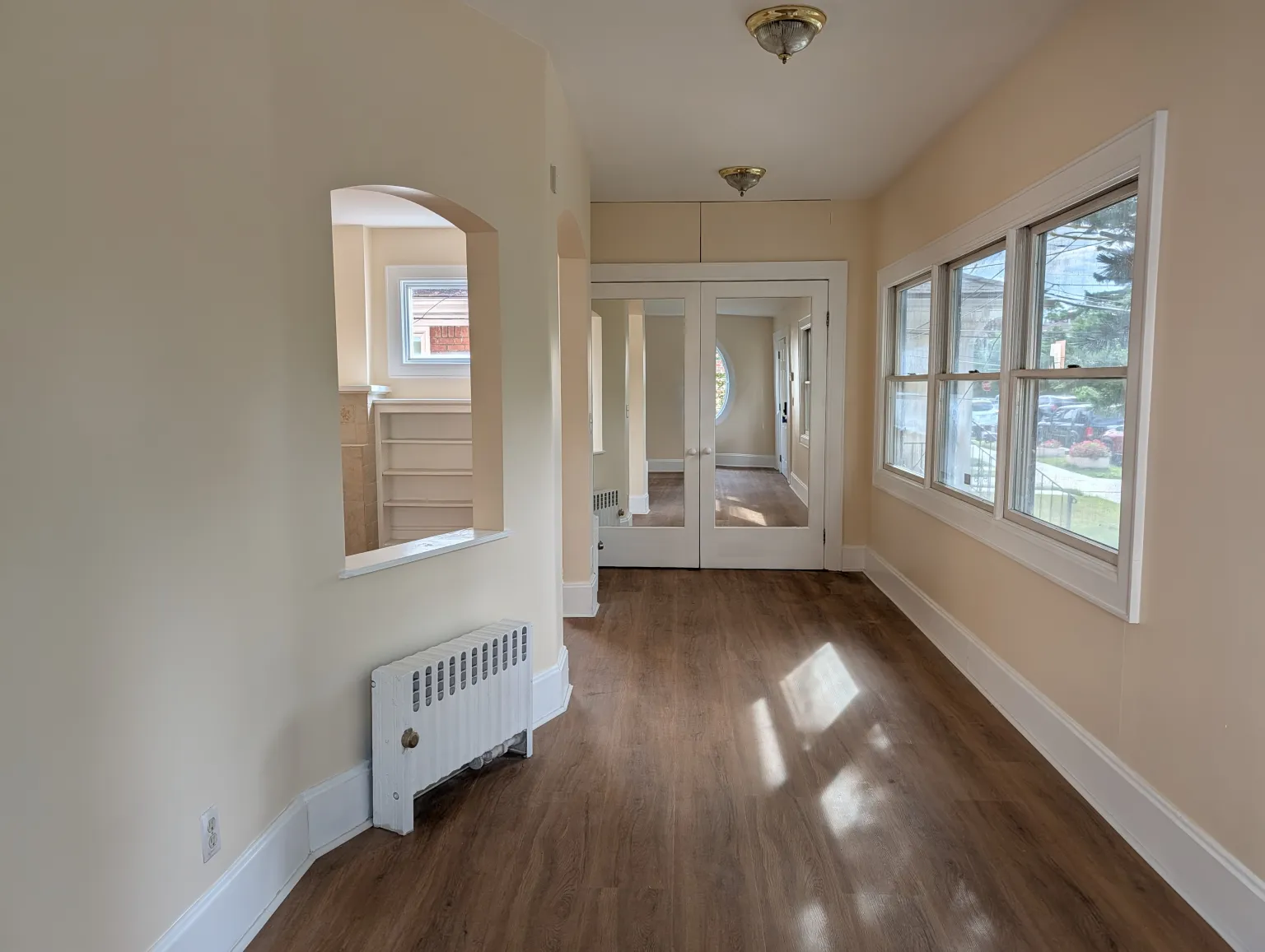 The length of the entry looking toward the mirrored French doors at the far end, with a bank of windows on one side and an archway through to the living room