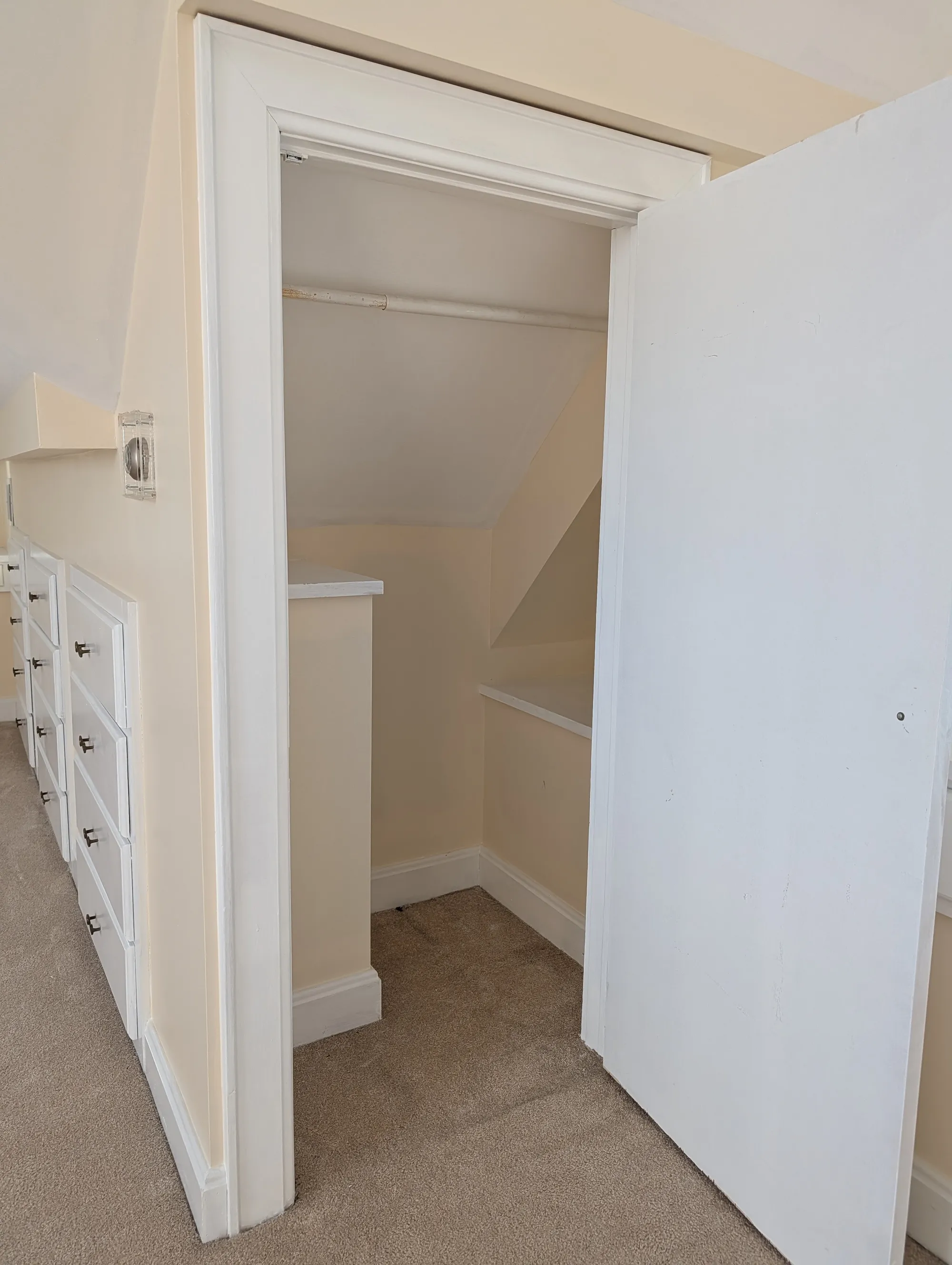 A closet opening beside the built-in chest of drawers on the suite floor, with a hanging rod inside and the bank of drawers alongside