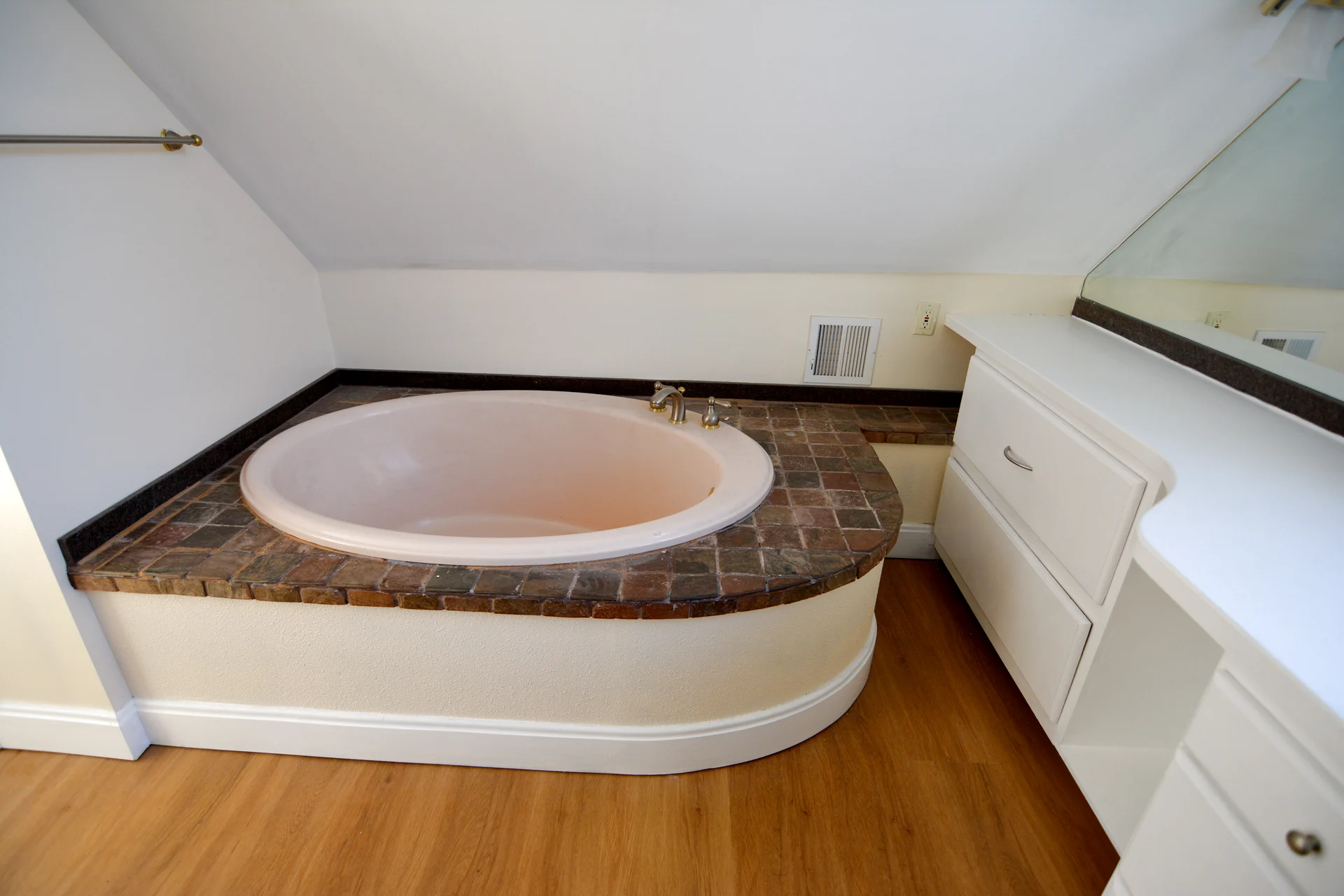 The soaking tub from the corner, peach oval tub set into a tiled surround beneath the eave, vanity drawers alongside
